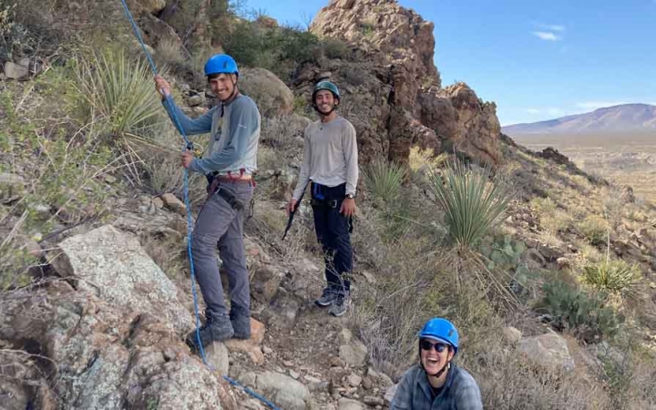 a group of gap year students smile while belaying rock climbers on an outward bound expedition 